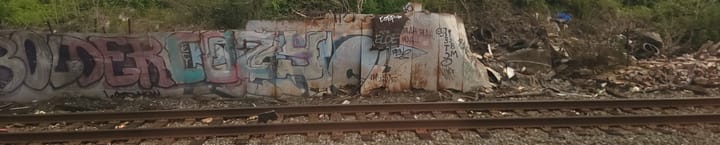 graffiti covering a ruined falling-down wall beside the garbage-strewn train tracks