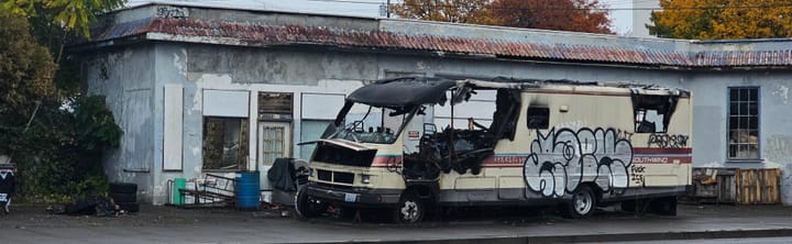 Burned-out trailer beside a shuttered storefront. 