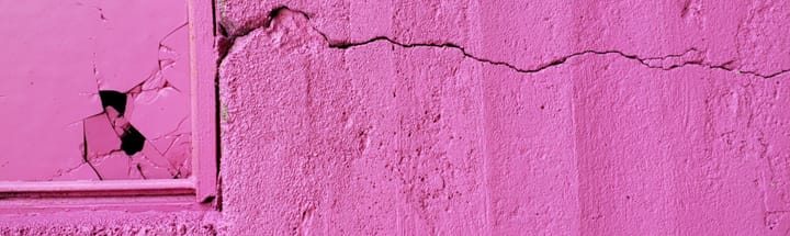 Pink-painted cracked wall with pink-painted broken window.