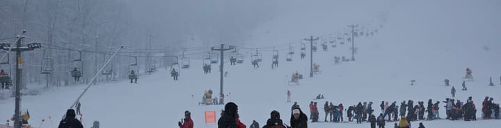 Ski mountain scene: people on a chairlift ascending into the fog; people waiting on line for the chairlift. 